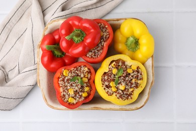 Photo of Quinoa stuffed bell peppers and basil in baking dish on white tiled table, top view