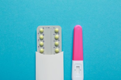 Photo of Birth control pills and pregnancy test on light blue background, top view. Space for text