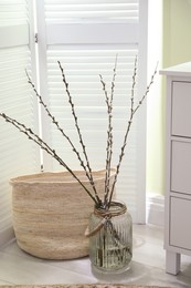 Photo of Glass vase with pussy willow tree branches on floor in room
