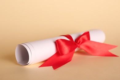 Photo of Rolled student's diploma with red ribbon on beige background