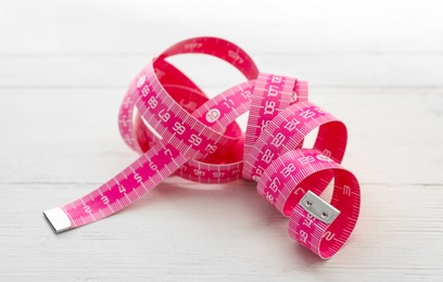 Pink measuring tape on white wooden table, closeup