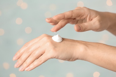 Woman applying hand cream on blurred background, closeup