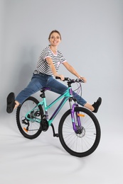 Happy young woman riding bicycle on grey background