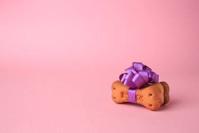 Bone shaped dog cookies with purple bow on pink background. Space for text
