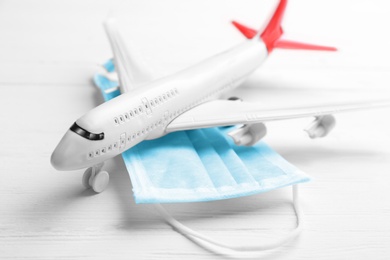 Toy airplane and medical mask on white wooden background, closeup. Travelling during coronavirus pandemic