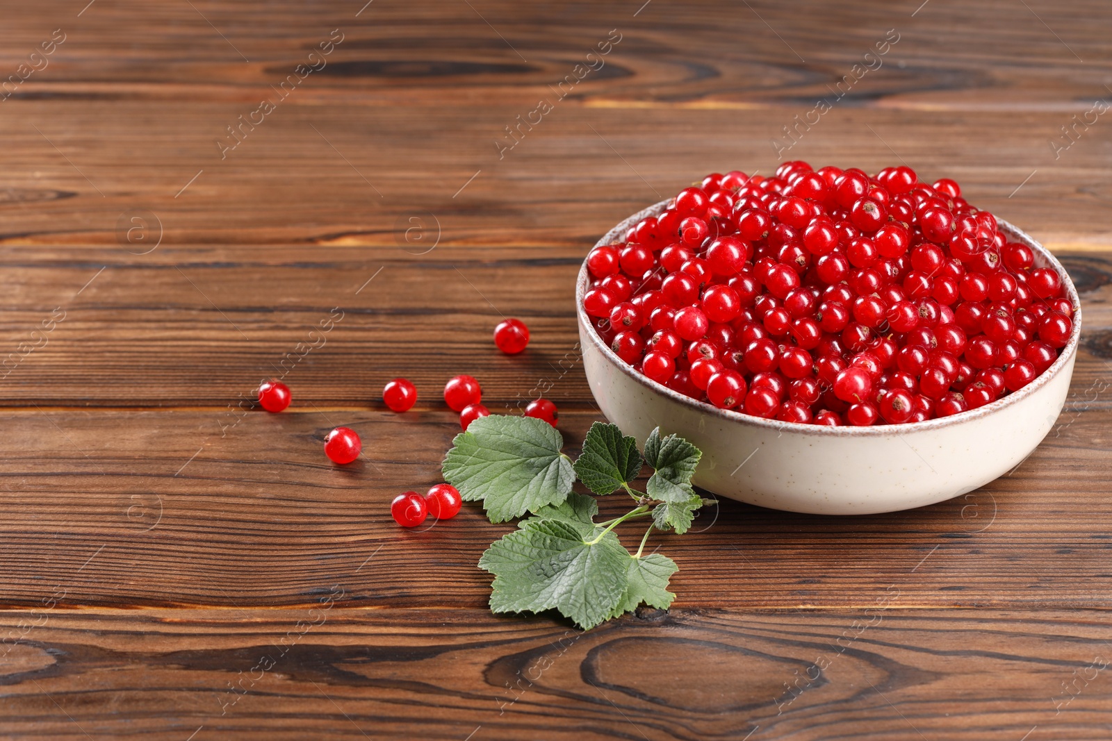 Photo of Ripe red currants and leaves on wooden table. Space for text