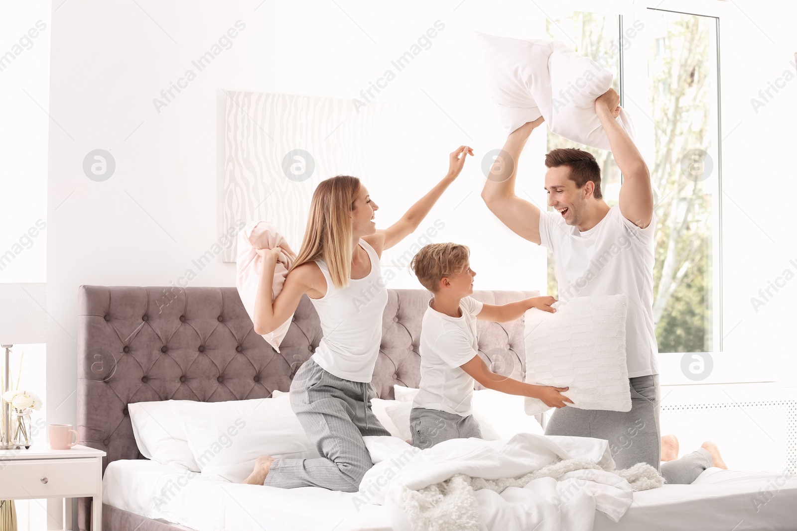 Photo of Happy family having pillow fight on bed at home