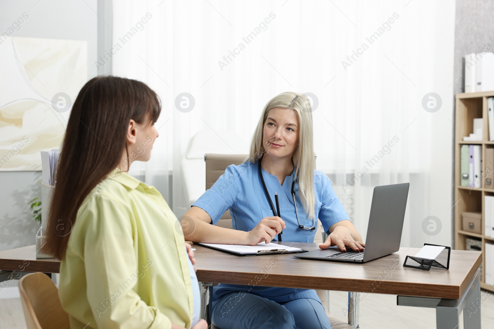 Photo of Doctor consulting pregnant patient at table in clinic