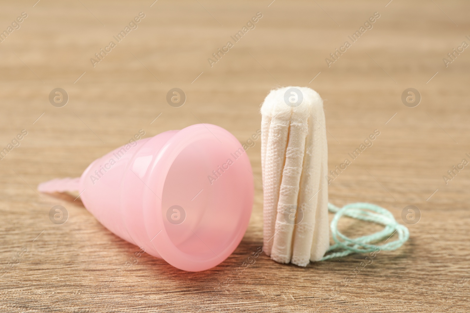 Photo of Menstrual cup and tampon on wooden table, closeup