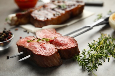 Photo of Fork with slices of grilled meat on grey table, closeup
