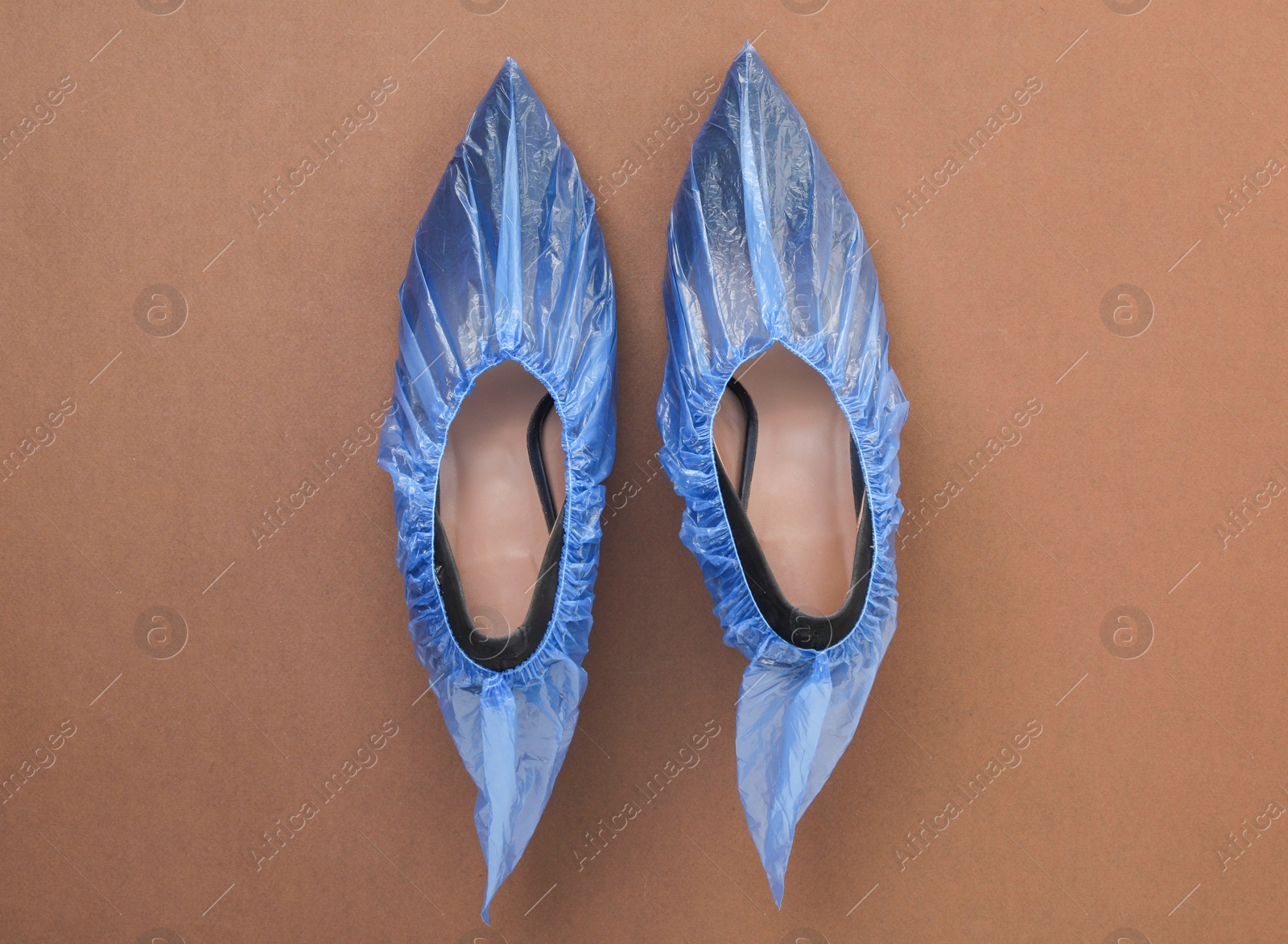 Photo of High heels in shoe covers on brown background, top view