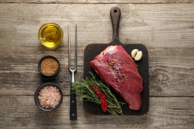 Photo of Piece of raw beef meat, rosemary, spices and fork on wooden table, flat lay