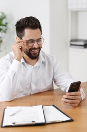 Photo of Handsome young man using smartphone at wooden table in office