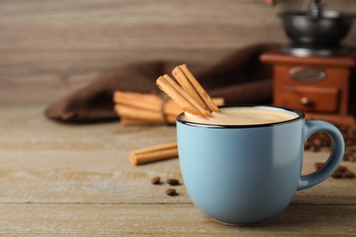 Photo of Cup of hot coffee with aromatic cinnamon on wooden table. Space for text