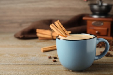 Cup of hot coffee with aromatic cinnamon on wooden table. Space for text