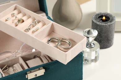 Photo of Jewelry box with many different accessories, perfume and burning candle on white table, closeup
