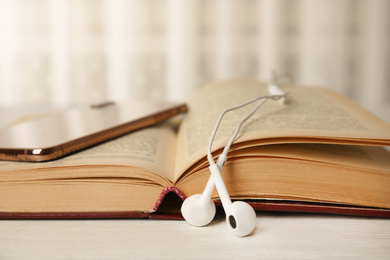Photo of Open book, earphones and mobile phone on white wooden table, closeup
