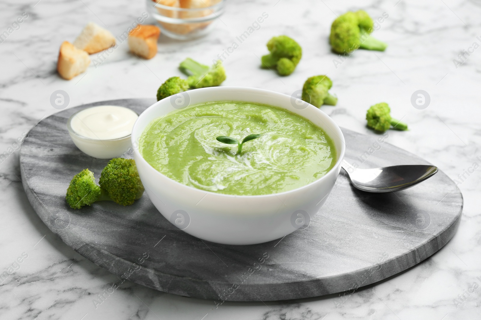 Photo of Bowl of broccoli cream soup served on white marble table