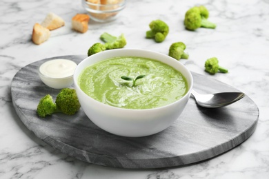 Photo of Bowl of broccoli cream soup served on white marble table