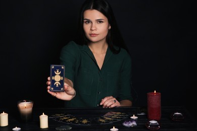 Soothsayer showing tarot card at table on black background. Fortune telling