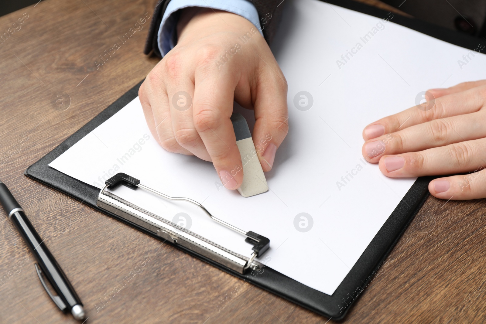 Photo of Man erasing something on paper at wooden table, closeup