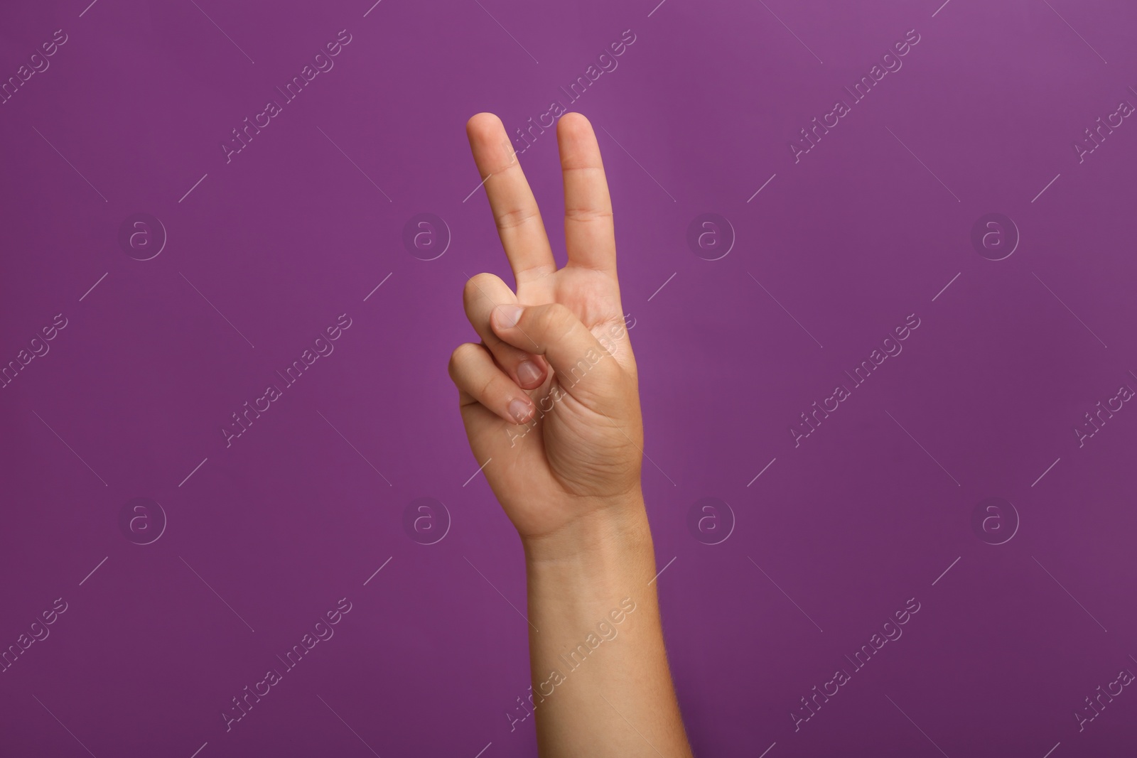 Photo of Teenage boy showing two fingers on purple background, closeup