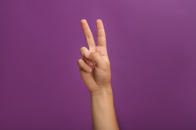 Photo of Teenage boy showing two fingers on purple background, closeup