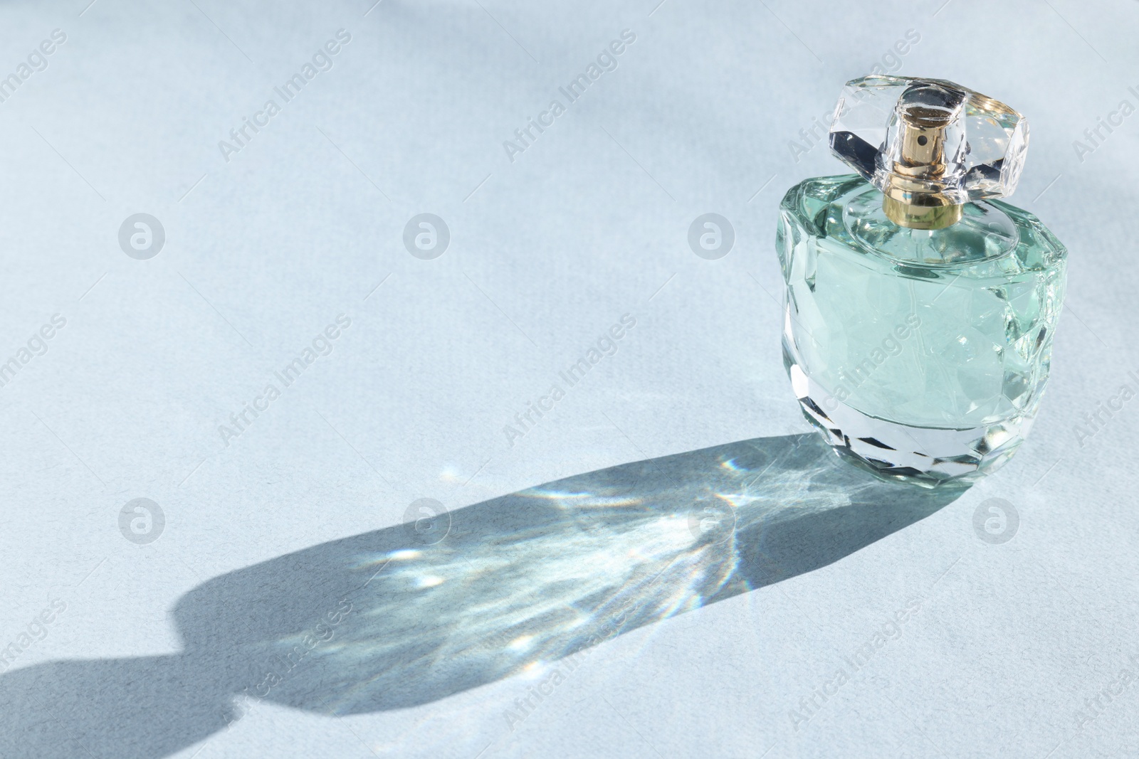 Photo of Luxury women's perfume. Sunlit glass bottle on grey background. Space for text