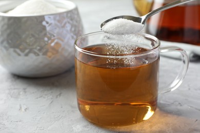 Photo of Adding sugar into cup of tea at grey textured table, closeup