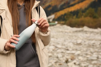 Photo of Woman holding thermo bottle in mountains, closeup. Space for text