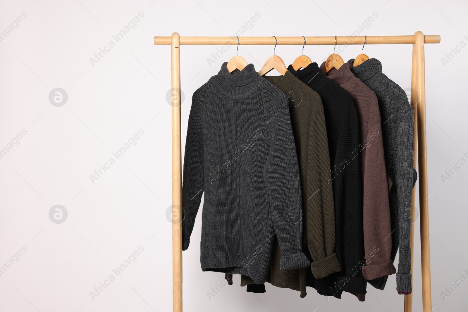 Photo of Rack with different casual sweaters on light background. Space for text