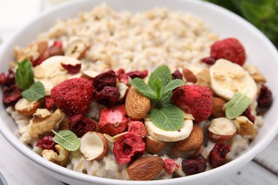 Photo of Delicious oatmeal with freeze dried berries, banana, nuts and mint in bowl, closeup