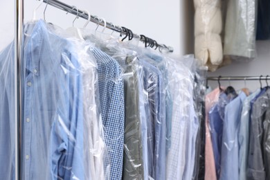 Photo of Dry-cleaning service. Hangers with different clothes in plastic bags on racks indoors, space for text