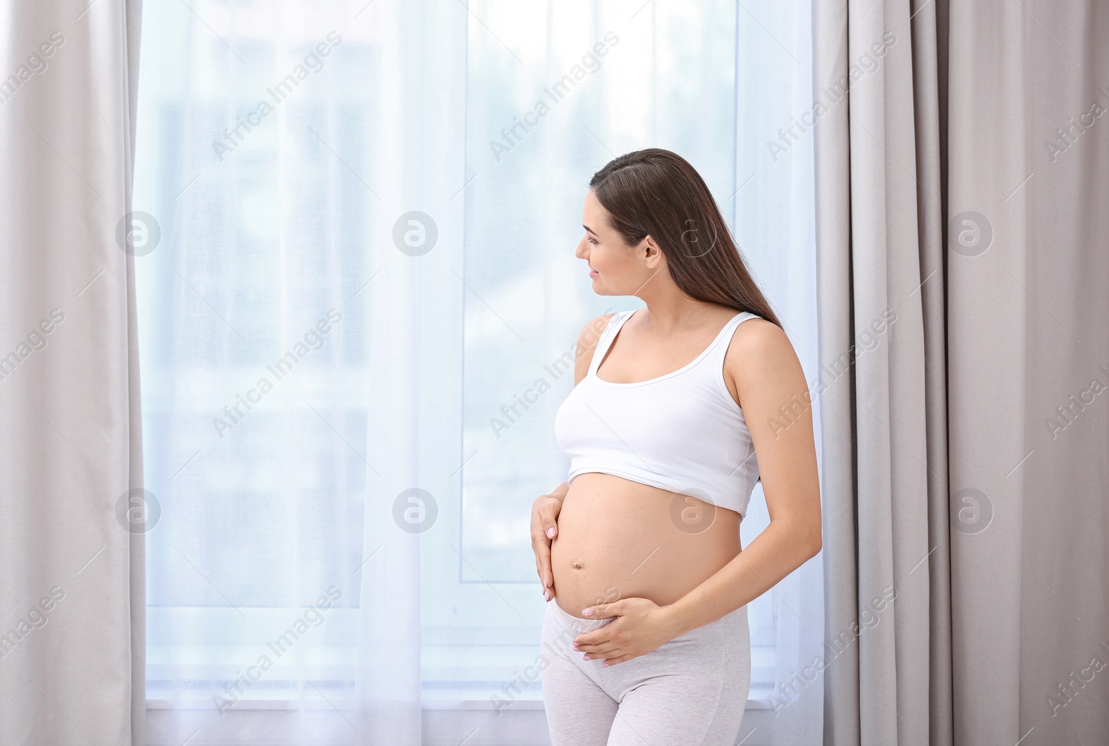 Photo of Young beautiful pregnant woman near window at home