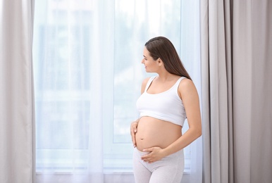 Young beautiful pregnant woman near window at home