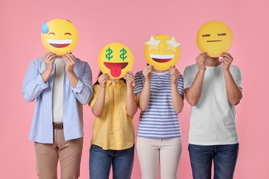 People covering faces with emoticons on pink background