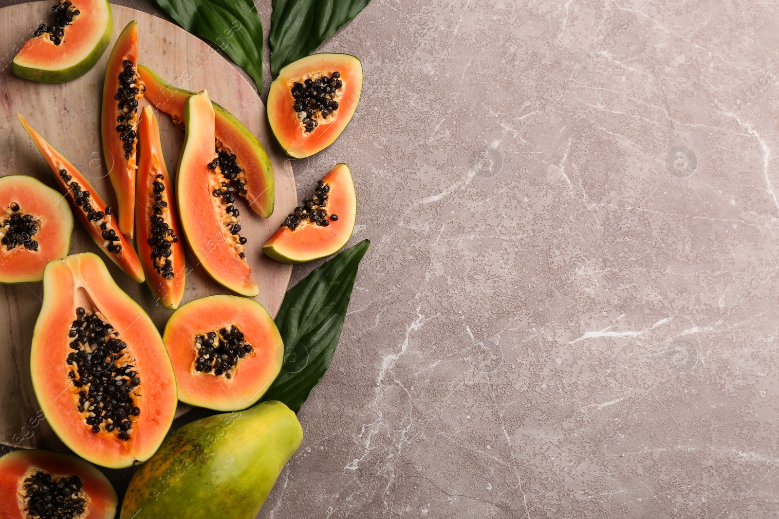 Photo of Fresh ripe papaya fruits with green leaves on grey table, flat lay. Space for text
