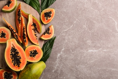 Fresh ripe papaya fruits with green leaves on grey table, flat lay. Space for text