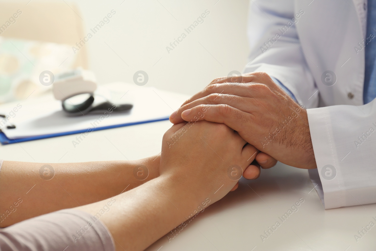Photo of Male doctor comforting woman at table, closeup of hands. Help and support concept