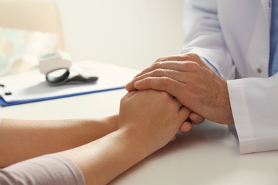 Photo of Male doctor comforting woman at table, closeup of hands. Help and support concept