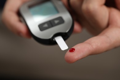 Photo of Diabetes test. Man checking blood sugar level with glucometer on blurred background, closeup