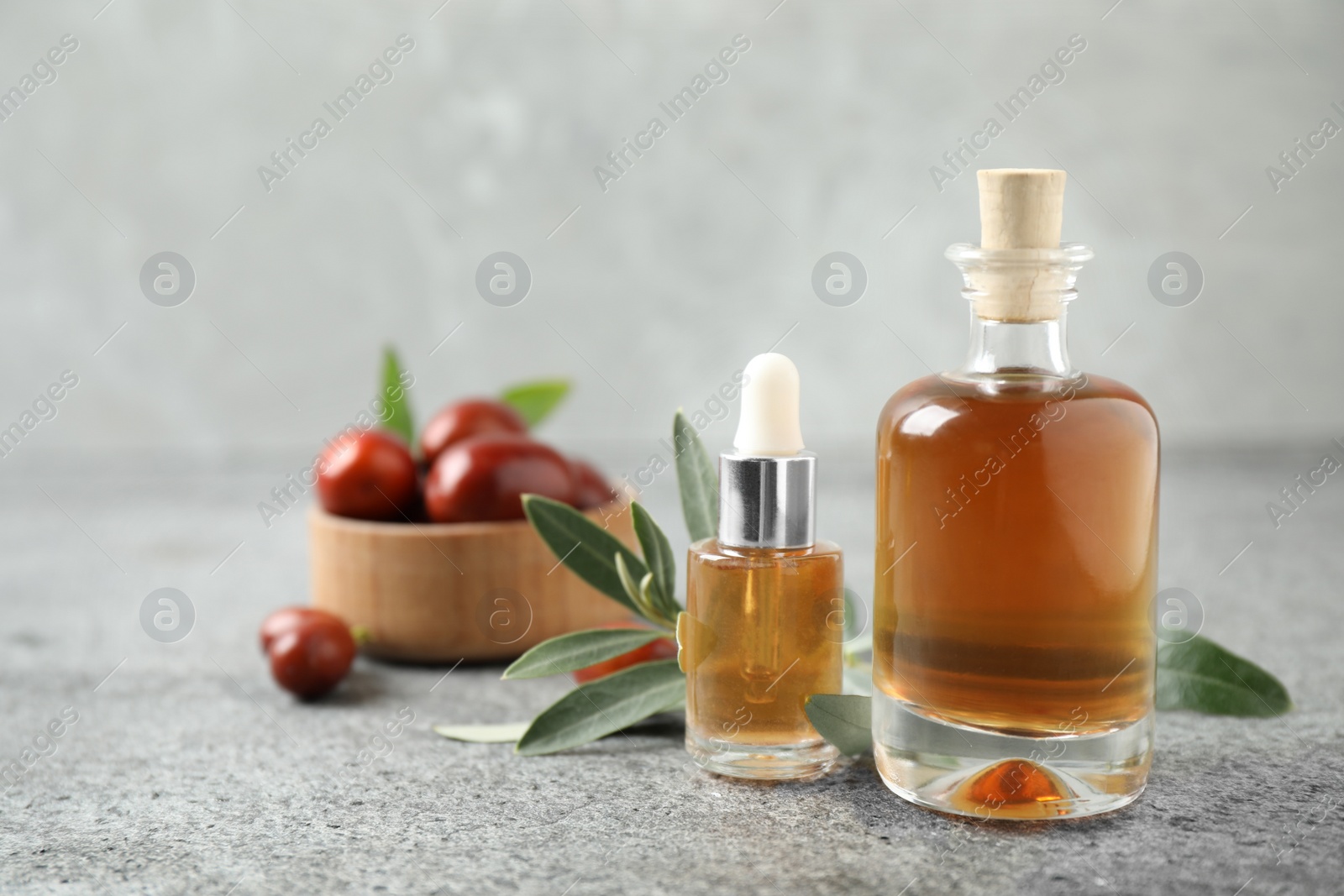 Photo of Glass bottles with jojoba oil on stone table against grey background. Space for text