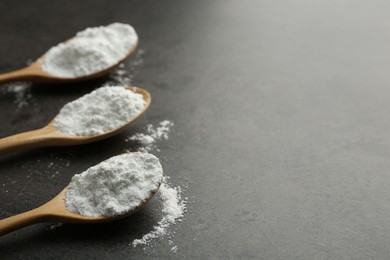 Photo of Baking powder in spoons on grey textured table, closeup. Space for text