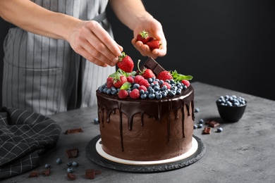 Photo of Woman decorating delicious chocolate cake with fresh strawberries at table, closeup