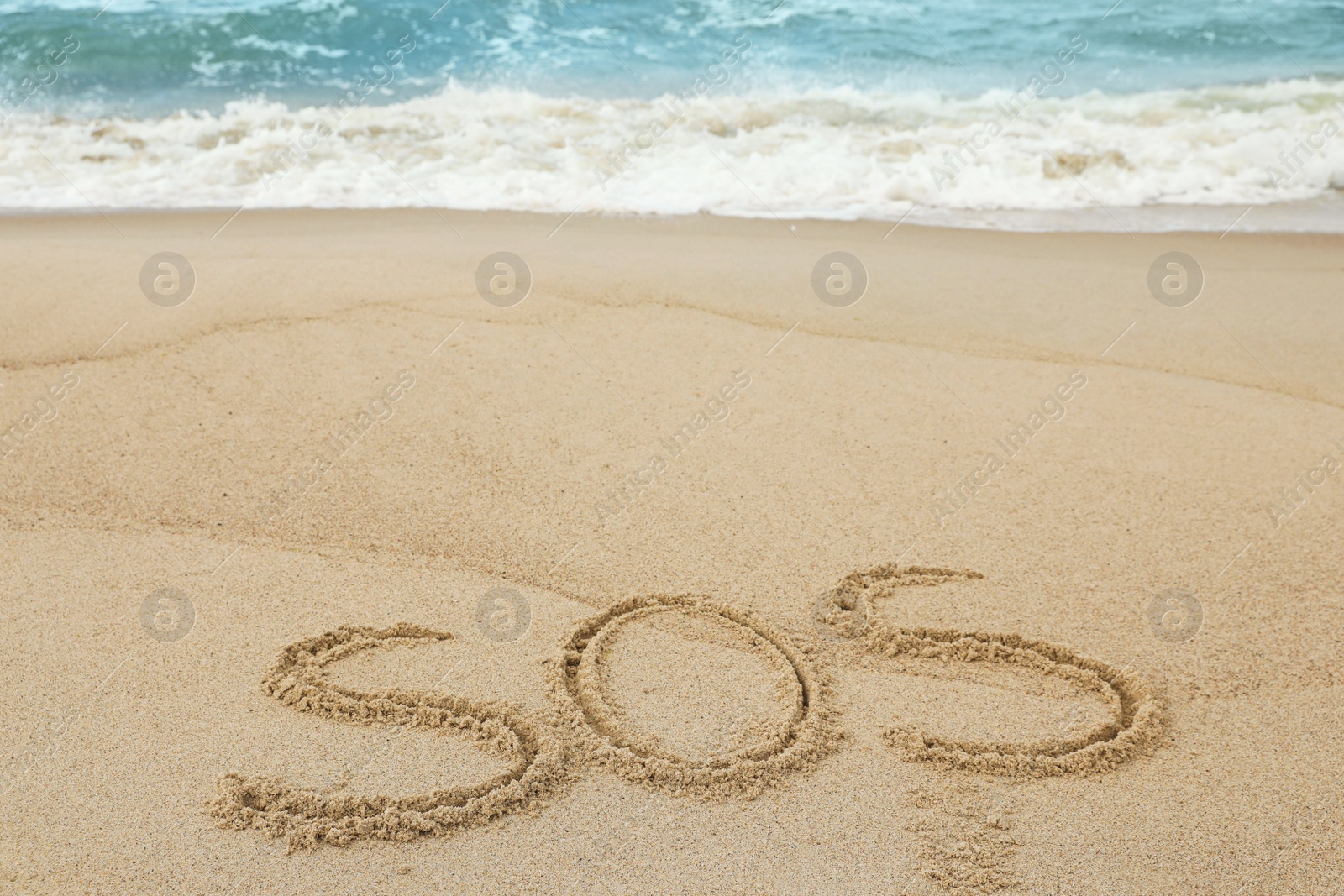 Photo of Message SOS drawn on sand near sea