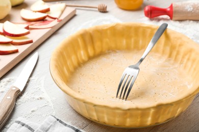 Photo of Raw dough with fork and ingredients on white wooden table. Baking apple pie