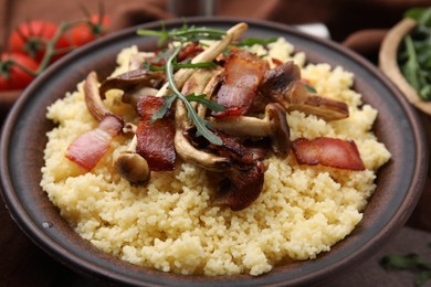 Tasty couscous with mushrooms and bacon in bowl on table, closeup