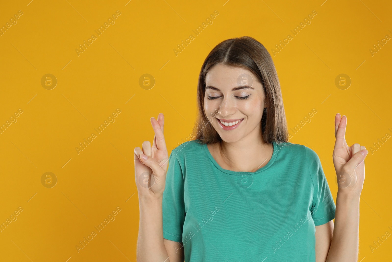 Photo of Woman with crossed fingers on yellow background, space for text. Superstition concept