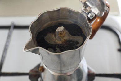 Brewing aromatic coffee in moka pot on stove, closeup