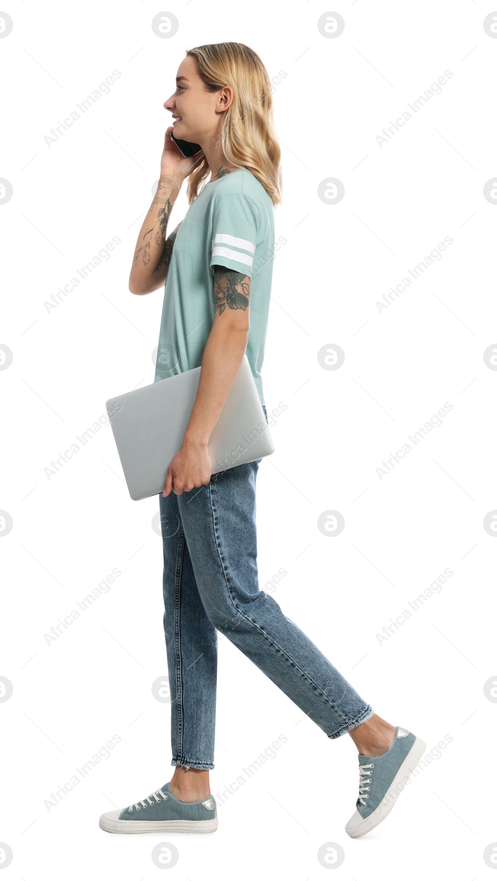 Photo of Young woman with laptop talking on smartphone and walking against white background